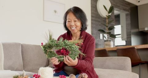 Senior Asian Woman Crafting Holiday Wreath in Cozy Living Room