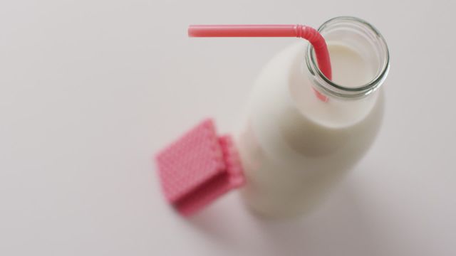 Glass bottle of fresh milk with a red straw next to pink wafers, placed on a clean white background. Ideal for promoting dairy products, organic nutrition, and healthy snack options. Suitable for food blogs, healthy lifestyle websites, and advertising natural products.