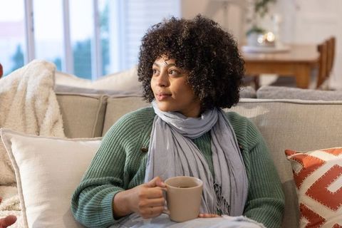 Cozy morning routine woman relaxing on sofa with mug and scarf by window