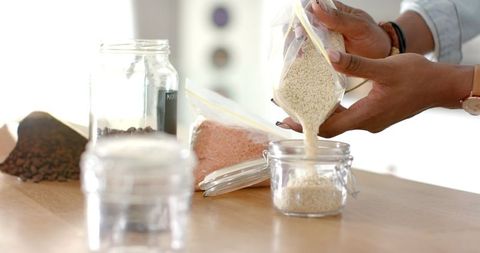 Woman organizing pantry by pouring rice into glass jar