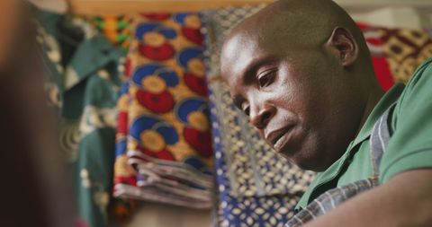 African Tailor Crafting Garments in Workshop with Colorful Fabrics Hanging