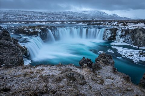 Cascading turquoise waterfall in icy volcanic landscape at dusk with snow-covered cliffs