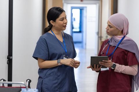 Nurses collaborating in hospital corridor consulting tablet, sharing patient information