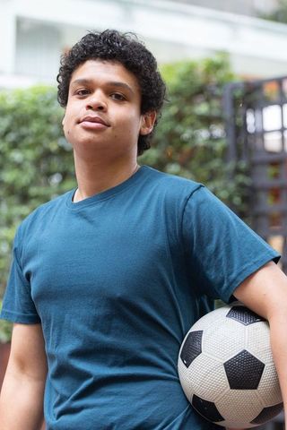 Teenager standing holding soccer ball looking confident in residential courtyard
