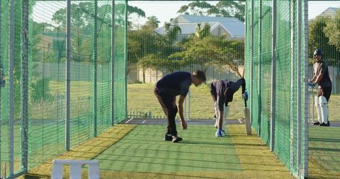 Cricket net practice with bowler delivering to batsmen wearing helmet, pads and gloves