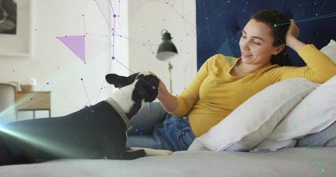 Smiling woman reclining on bed petting black and white dog with digital network overlay