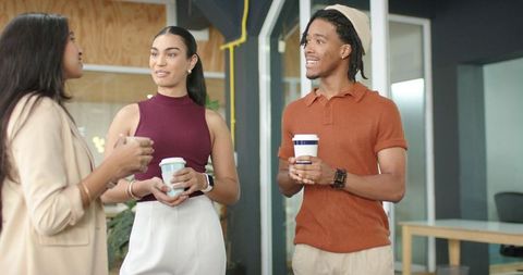 Diverse coworkers chatting while holding takeaway coffee in modern office lounge