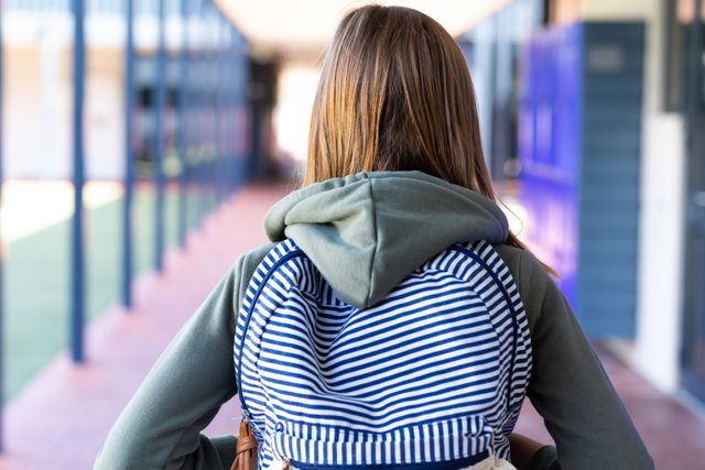 Caucasian girl with a striped schoolbag walking down an elementary school corridor. Ideal for use in educational materials, back-to-school promotions, and childhood learning resources.