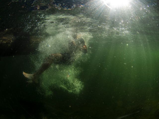Person diving into green water creating a splash with bubbles, and sunlight streaming from above. Useful for water sports ads, adventure activities, or summer vacation themes.