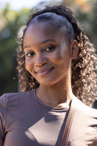 African american woman smiling in park wearing athletic top crossbody bag curly headshot