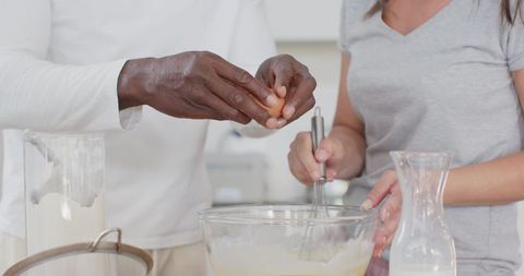Couple baking together cracking egg and whisking batter in bright sunlit home kitchen