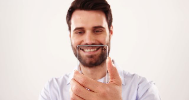Man smiling while holding a transparent glass square, focusing on the futuristic object in his hand. Suitable for concepts related to technology, innovation, future technology ideas, and creative or tech-focused projects. Ideal for advertisements, website banners, and promotional materials highlighting modern technology and innovative products.