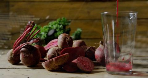 Pouring beet juice into tall glass with fresh halved beets on rustic wooden table