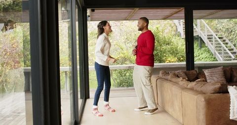 African american couple chatting by glass doors in modern living room with garden view