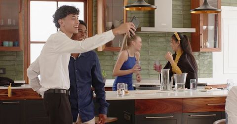Diverse friends posing for selfie in modern sunlit kitchen, laughing and sipping drinks