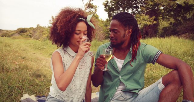 A young African American couple enjoys a romantic picnic outdoors, with copy space. They share a moment of connection over a glass of wine, surrounded by natural scenery.
