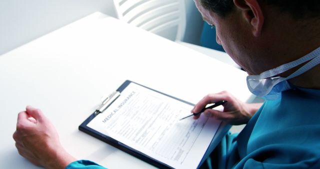 Medical professional is filling out insurance paperwork at desk, indicating busy healthcare environment. Can be used for health insurance companies, medical blogs, or articles discussing healthcare administration and claims process.