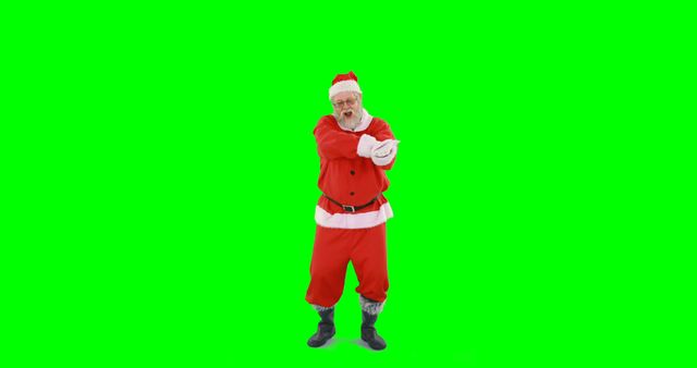 A Caucasian senior man dressed as Santa Claus stands with arms crossed against a green screen background, with copy space. His cheerful expression and festive costume add a touch of holiday spirit to the image.