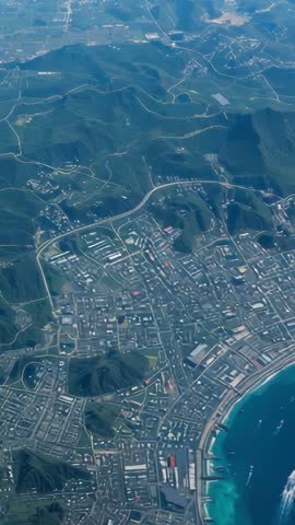 Vertical aerial video capturing coastal city grid, mountain ridges and vessel wakes