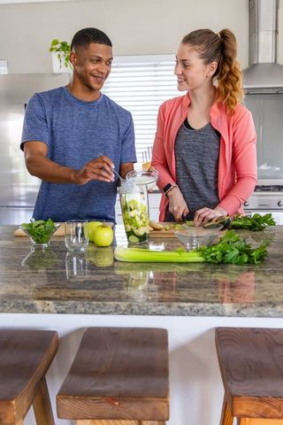 Mixed-race couple preparing green smoothie on kitchen island, healthy home lifestyle