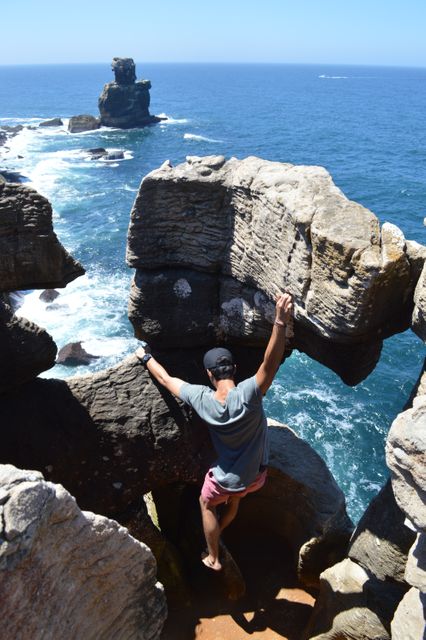 Man standing on rocky coastal cliff overlooking ocean, capturing sense of adventure and exploration. Perfect for use in travel blogs, adventure lifestyle content, outdoor apparel promotions, and motivational posters emphasizing freedom and nature.