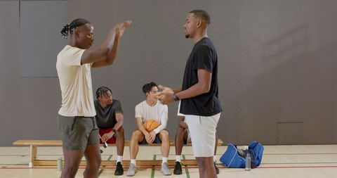 African american men shaking hands on indoor basketball court while teammates resting