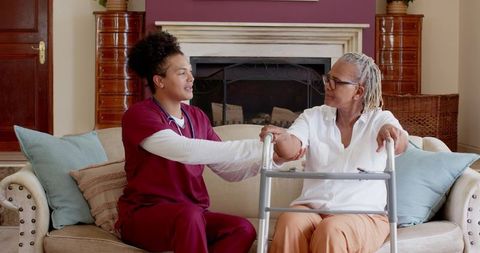 Caring nurse assisting senior woman at home with walker support