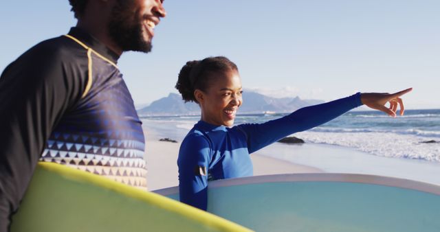 African american couple talking and carrying surfboards on the beach. holiday and healthy outdoor leisure time by the sea.