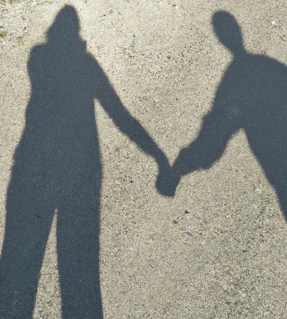 Silhouetted shadows of a couple holding hands are cast on a sunlit pavement, creating an artistic and romantic scene. This image can be used to depict themes of love, connection, partnership, and companionship. Suitable for relationship advice websites, engagement announcements, or any project celebrating unity and togetherness.