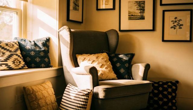 Cozy wingback armchair basking in warm sunlight with patterned pillows and window seat