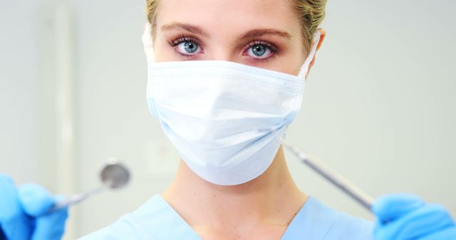 Female dentist in scrub uniform holding dental instruments, ready for patient treatment. Ideal for use in dental care advertisements, healthcare industry articles, and professional health service websites.