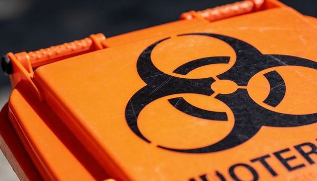 Closeup orange hazardous waste lid showing black biohazard trefoil symbol and scratched texture