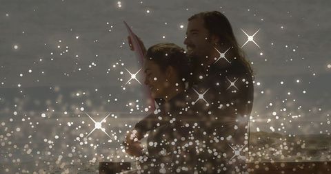 Couple Hugging at Shoreline Holding Pink Surfboard at Dusk with Sparkling Bokeh Lights