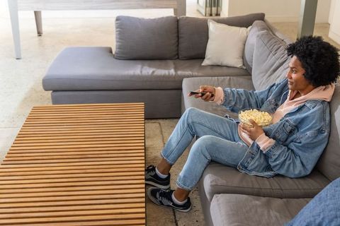 African american man lounging on contemporary gray sectional holding popcorn and remote