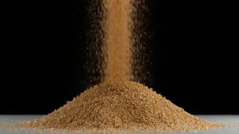 Pouring golden semolina settling into symmetrical pile in slow motion on dark background
