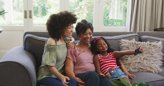 Happy biracial mother, daughter and grandmother sitting on couch taking selfie with smartphone - Download Free Stock Photos Pikwizard.com