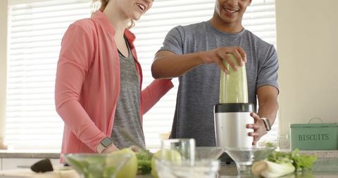 Young couple making green smoothie in modern kitchen with african american man blending