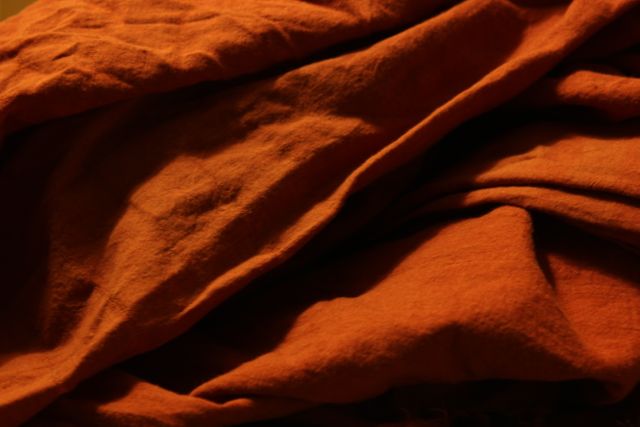 Detailed close-up of wrinkled orange fabric under warm lighting. Ideal for backgrounds, textile industry, design projects, and material texture illustrations in fashion or home decor.