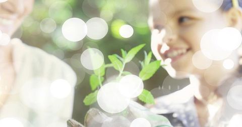 Senior woman and girl planting seedling in garden with sunlit bokeh, smiling and bonding