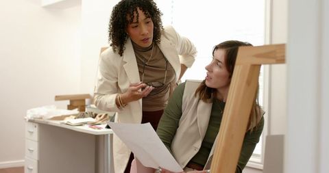 Diverse women designers collaborating in modern studio reviewing fabric swatches, sketches