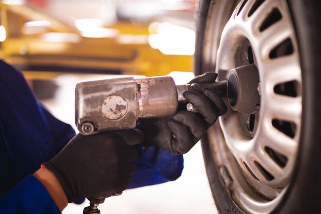 Female mechanic unbolting car wheel in a garage. Ideal for illustrating automotive services, car maintenance, and professional mechanics. Useful for promoting car repair shops, independent business owners, and mechanical workshops.
