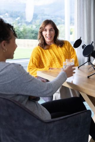 Two women recording podcast interview in bright home studio with microphones