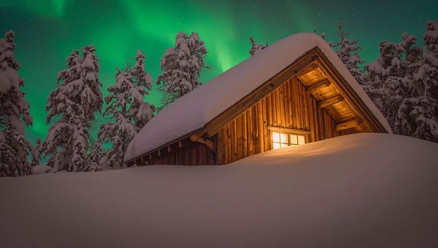 Warm-lit rustic cabin under vivid northern lights on deep snowdrift for cozy winter escape