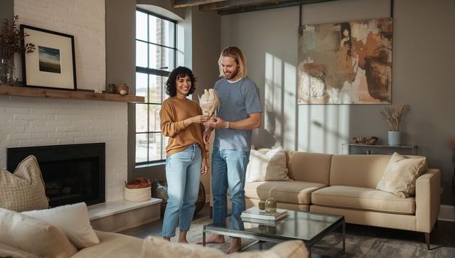 Couple examining wooden sculpture in sunlit modern loft living room with neutral decor