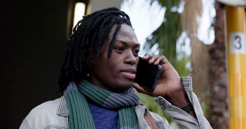 African american man talking on smartphone outdoors wearing denim jacket scarf urban