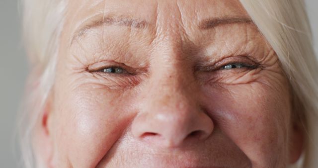 Close-up of a smiling elderly woman showing wrinkles and facial lines, eyes almost closed and a happy expression indicating joy and warmth. Ideal for use in articles about aging gracefully, senior portraits, skincare for mature skin, and emotional well-being in older age.
