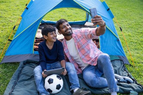 Father and Son Camping with Gadgets and Soccer Ball Outdoors