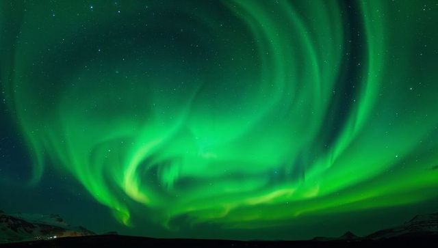 Emerald aurora dancing over Arctic mountains with starlit night and distant lights