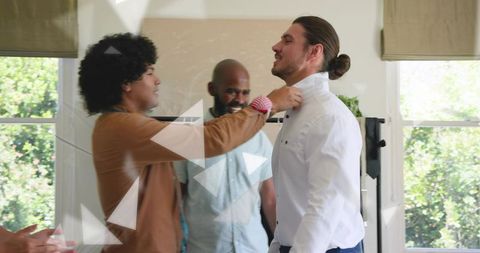 Stylist adjusting collar on man with man bun while team preparing semiformal wardrobe