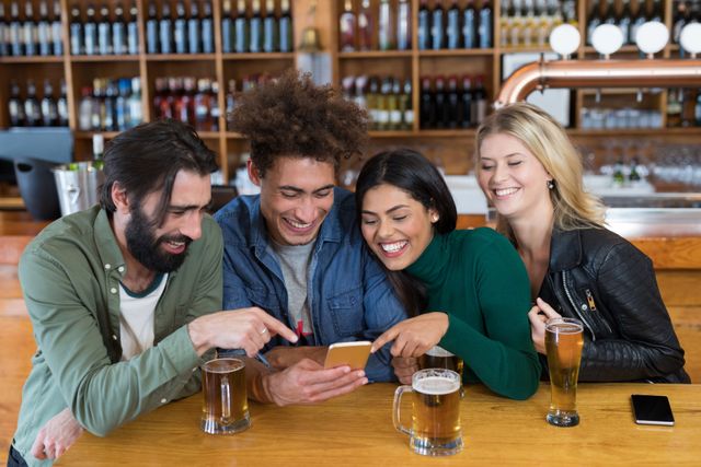Group of friends sitting at bar counter, enjoying beer and sharing moments on mobile phone. Perfect for themes related to friendship, social gatherings, nightlife, technology in social settings, and leisure activities.